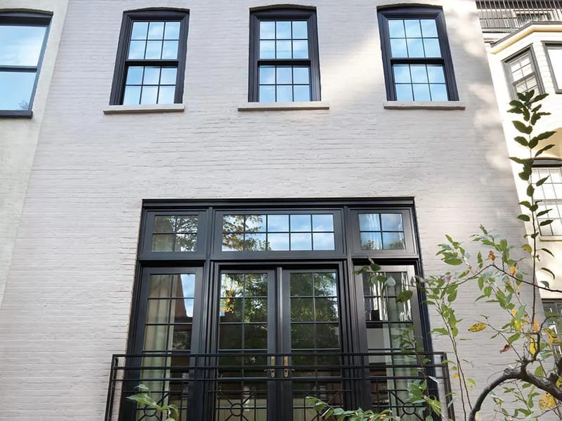 Black-framed windows and a transom set into a painted white brick facade