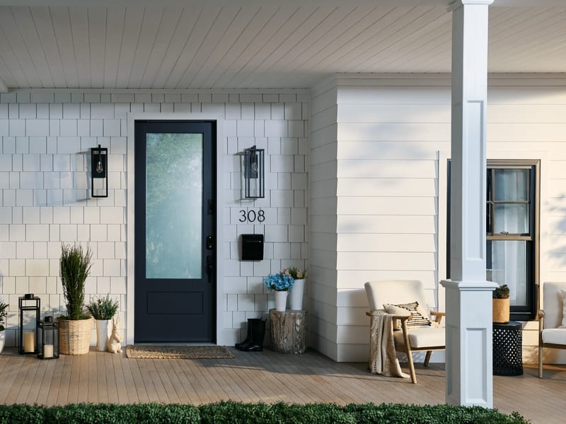 A black entry door with a full obscure-glass panel on a white shingled porch