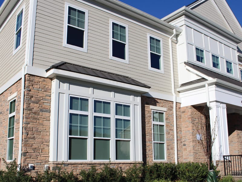 A two-storey window bay with white frames set into brick and siding