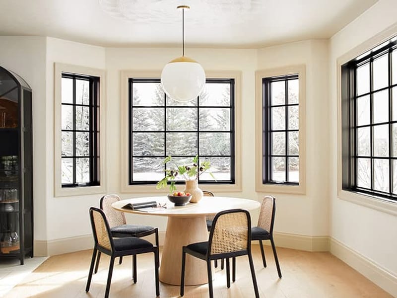A black-framed bay window with divided lights above a round dining table