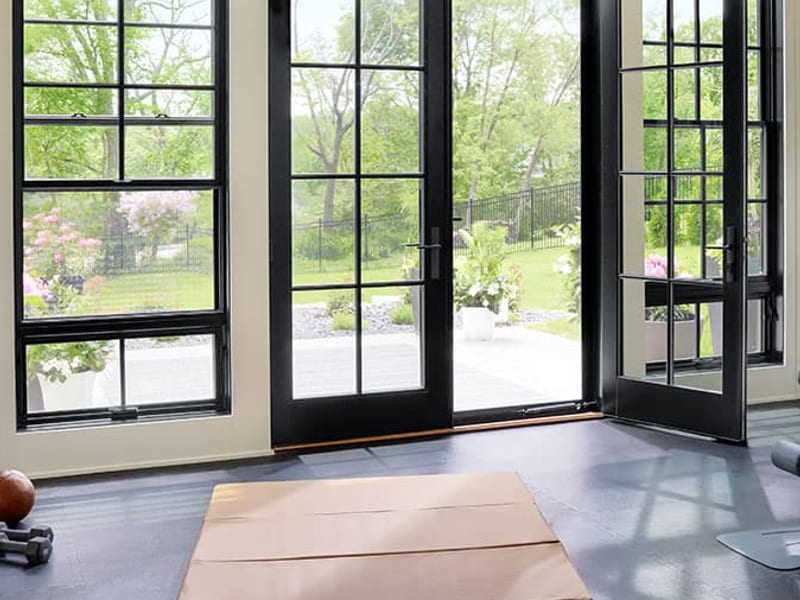 Black hinged patio doors with divided lights standing open onto a lawn