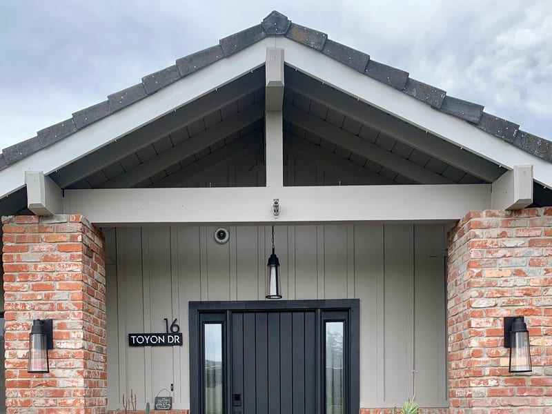 A black entry door with a full-height glazed sidelight under a gabled porch