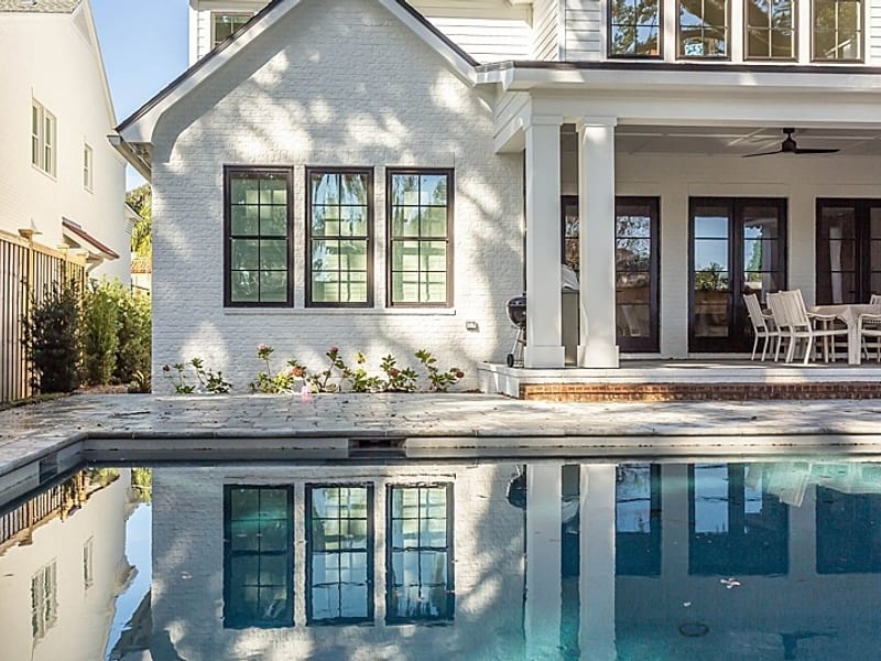 Black-framed windows in a white brick elevation reflected in a pool